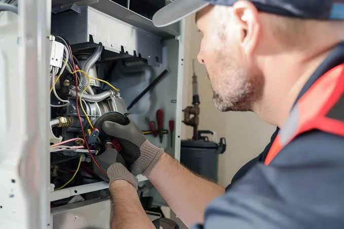 Illustrative close-up of a gloved technician checking furnace wiring and components